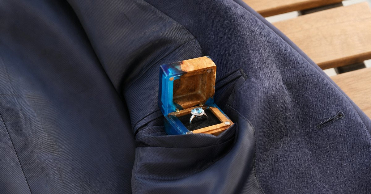 Open blue wood and resin engagement ring box concealed in a navy jacket pocket