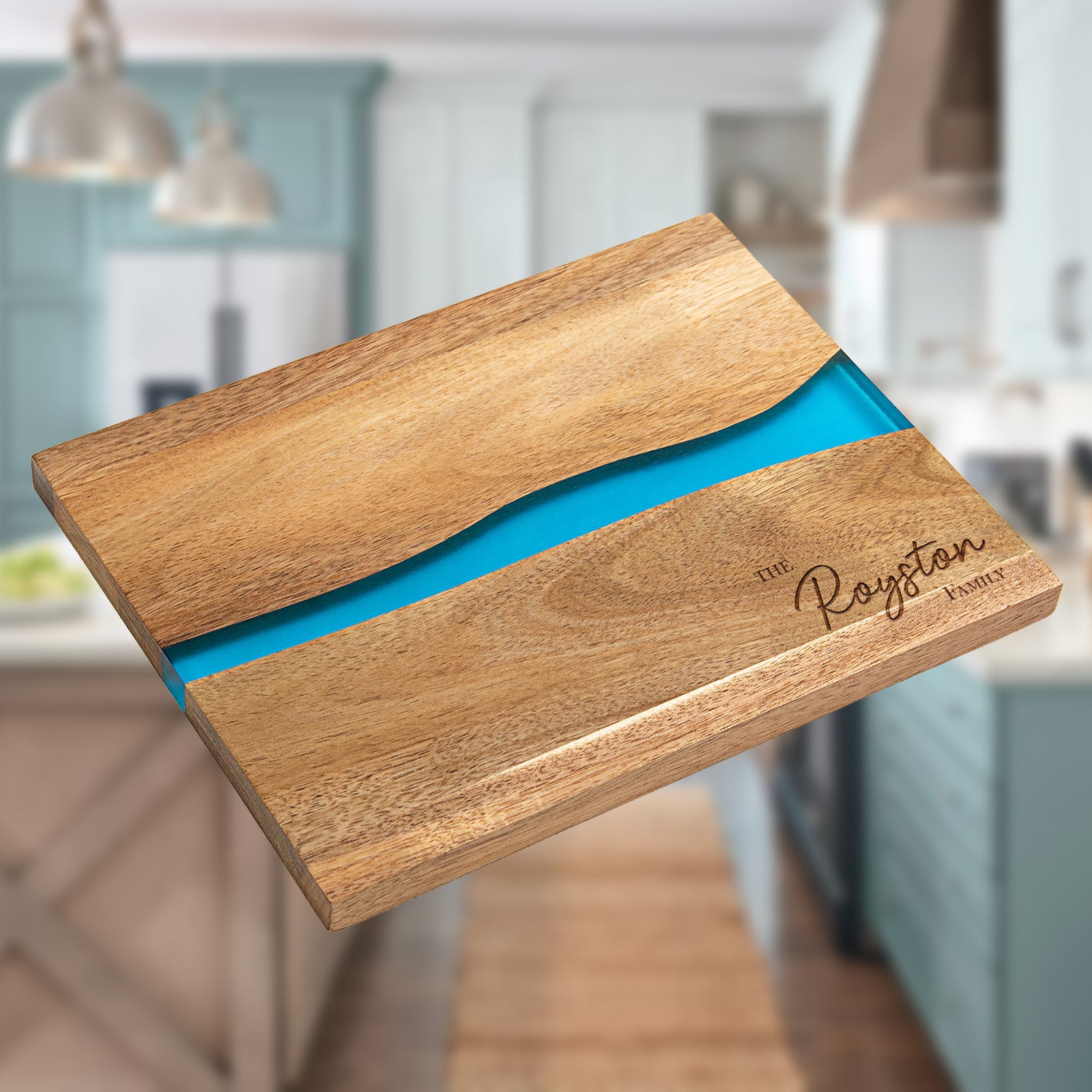 Flat lay view of personalized epoxy resin cutting board with The Royston Family script engraving on acacia wood and blue river resin inlay